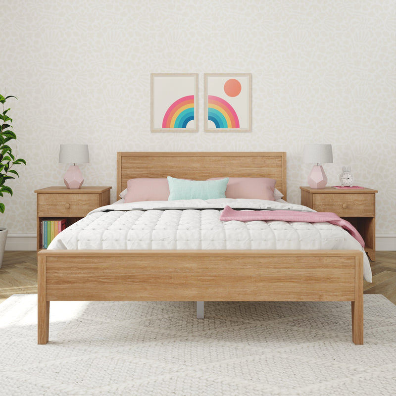 Modern bedroom interior with wooden platform bed, white quilted comforter, pastel pink and mint pillows, matching wooden nightstands with pink geometric lamps, potted plant, bunny alarm clock, and two framed rainbow prints on cream patterned wallpaper