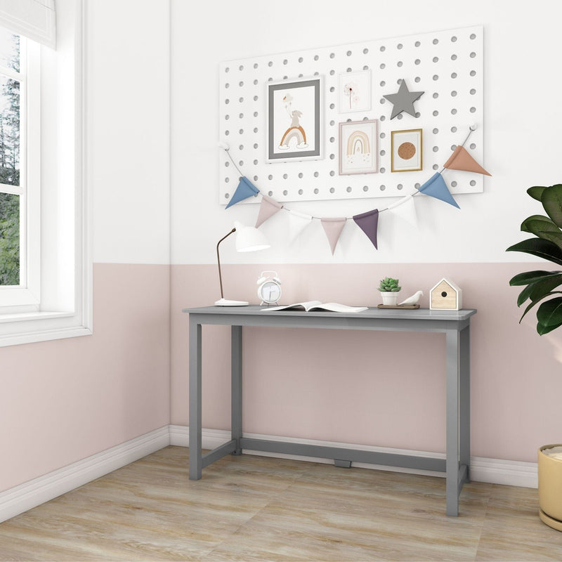 Small gray kids study desk in pastel pink-and-white nursery with pegboard gallery, colorful bunting, desk lamp, alarm clock, succulent and wooden birdhouse on light wood floor