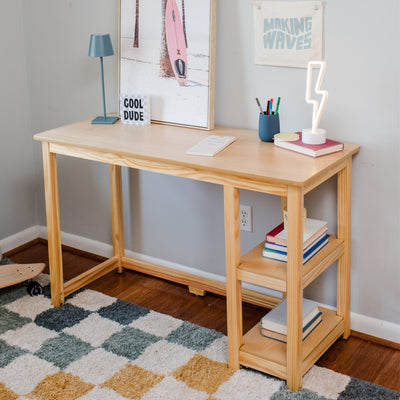 Small light pine wood desk with open shelves, books and neon lightning lamp — modern kids' bedroom study desk and home office nook with surfboard wall art and checkered rug