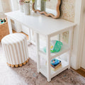 White children's vanity desk with scalloped mirror, striped round ottoman, mint green trucker hat and stacked children's books on lower shelves styled on a floral nursery rug