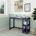 Compact navy blue writing desk with open side shelves in a minimalist home office with mint green two-tone walls, pegboard storage, table lamp, potted plant and framed rainbow artwork lit by window natural light.
