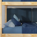Close-up of lower bunk bed with natural wood frame, layered blue bedding, navy textured cushions and gingham pillow