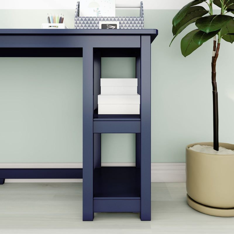 Navy blue desk with open shelves and stacked white storage boxes beside a potted plant on hardwood floor in a minimalist mint-green home office