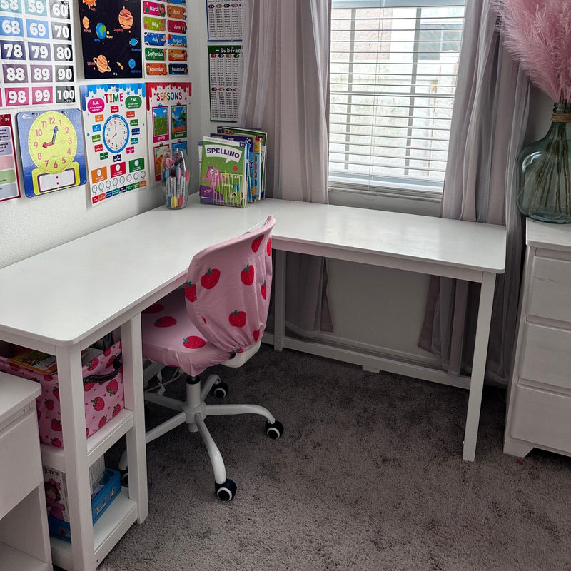 Children's study nook with white L-shaped desk, pink strawberry-covered swivel chair, colorful educational wall posters and spelling books by a sunlit window
