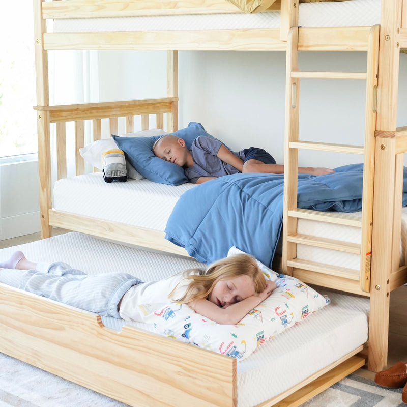 Children sleeping on a wooden bunk bed and trundle with blue bedding in a bright bedroom.