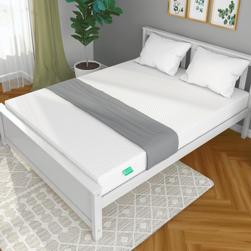 Modern bedroom with a comfortable white mattress on a sleek bed frame, accented by green plants and stylish decor.