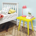 Bright yellow bedside table with a pink lamp, books, and a succulent plant next to a white bed in a modern bedroom with wooden flooring.