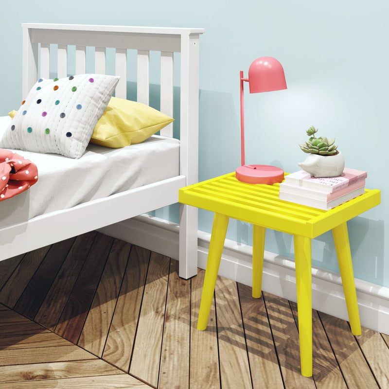 Bright yellow bedside table with a pink lamp, books, and a succulent plant next to a white bed in a modern bedroom with wooden flooring.