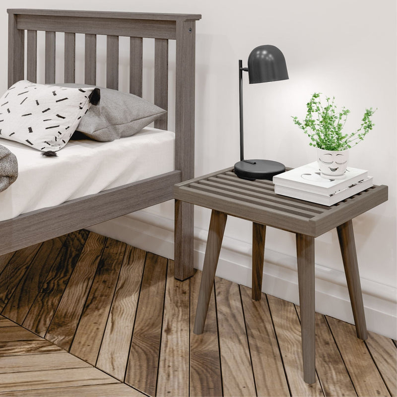 Gray wooden bed with a striped pillow and modern nightstand featuring a black lamp and plant, set on a polished hardwood floor.