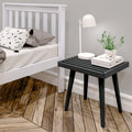 Modern bedroom with white bed, stylish black side table, and contemporary table lamp on wooden floor for cozy interior design.