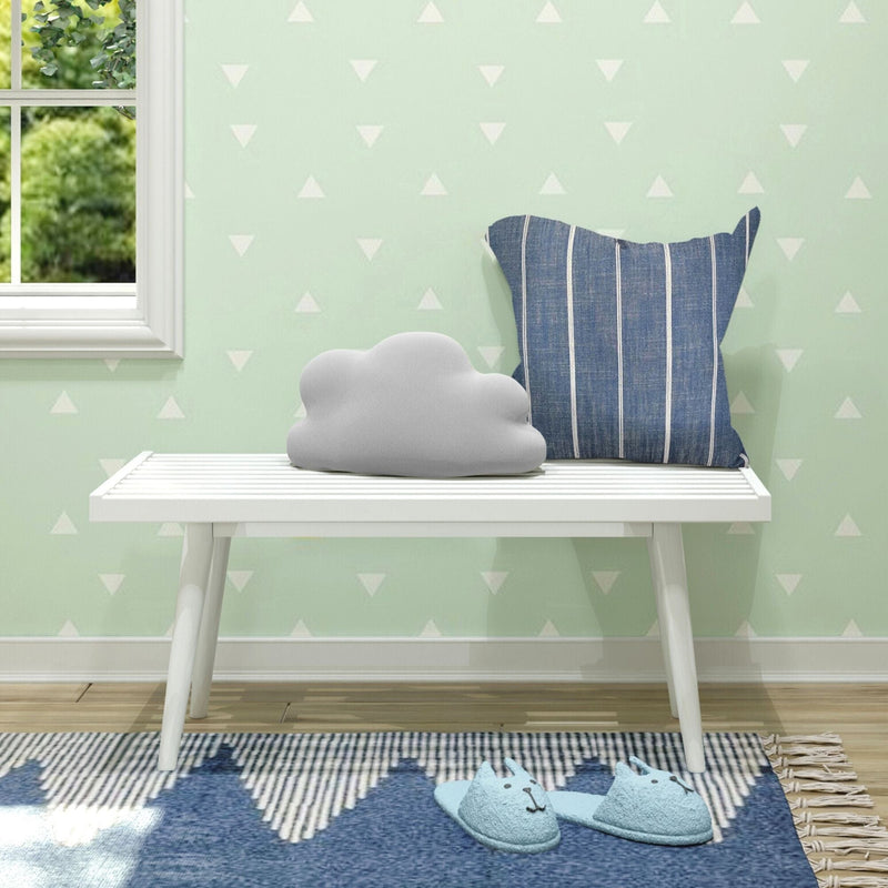 Cozy nursery room with cloud-shaped pillow, striped cushion, and adorable animal slippers on a white bench against a minimalist wallpapered wall.