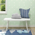 Cozy nursery room with cloud-shaped pillow, striped cushion, and adorable animal slippers on a white bench against a minimalist wallpapered wall.