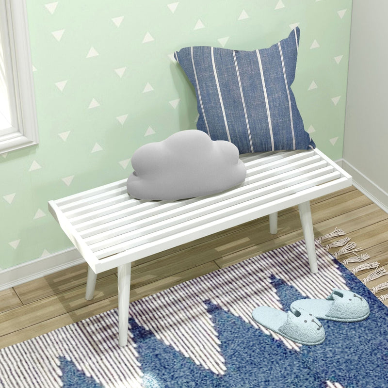 Cozy corner with white bench, cloud pillow, striped cushion, and blue slippers on a decorative rug.