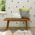 Stylish minimalist interior with wooden bench, cloud cushion, striped pillow, and cat slippers on patterned rug.
