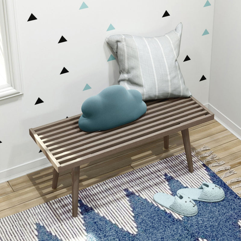 Cozy modern room decor with striped cushion, cloud pillow, wooden bench, and slippers on geometric rug.