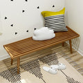 Minimalist room corner with wooden bench, decorative pillows, and cozy indoor slippers on a modern patterned rug.