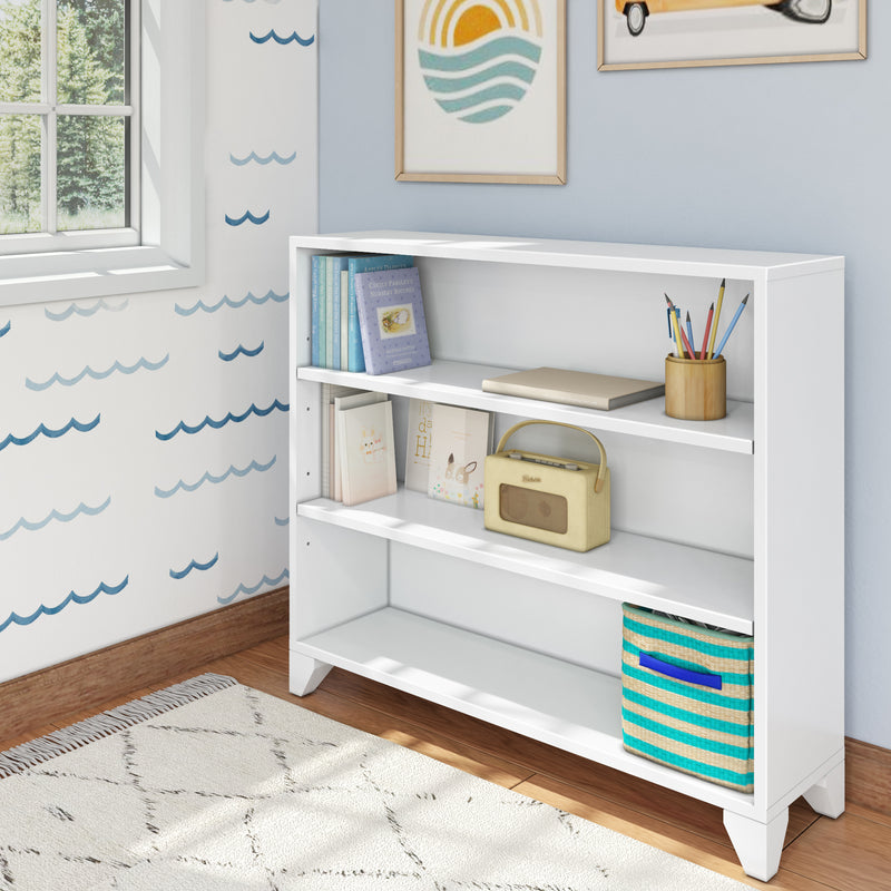 White wooden bookshelf in a modern room, holding books, a vintage radio, and colorful pencils, with wall art and wavy wallpaper for a stylish decor.