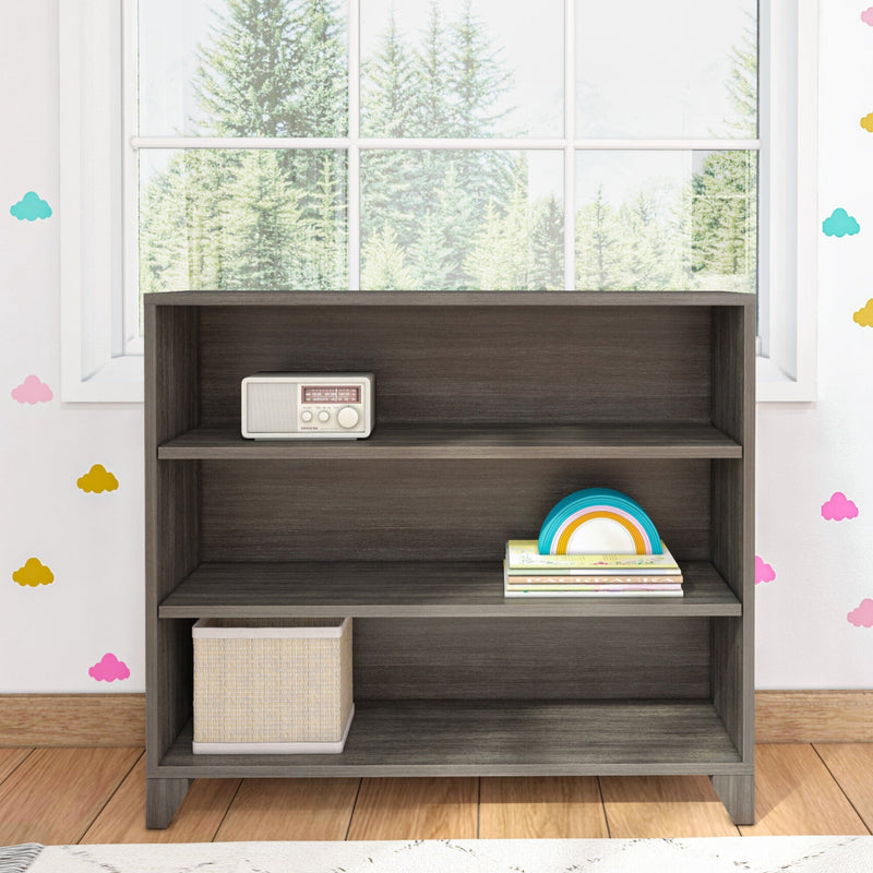 Modern wood bookshelf with three shelves, featuring a vintage radio and storage basket, in a room with colorful wall decorations.