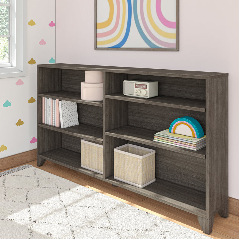 Gray wood open bookcase with cubby shelves, woven storage bins, children's books and rainbow toy in a pastel nursery room