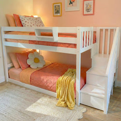 White wooden bunk bed with staircase, coral-pink bedding, daisy accent pillow and yellow throw in a pastel pink kids' bedroom with floral wall art — space-saving girls' bunk bed and kids room decor