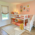 White wooden bunk bed with stairs in a pink and peach kids' bedroom with coral bedding, daisy pillow, floral wall art and scalloped jute rug — modern girls' room decor