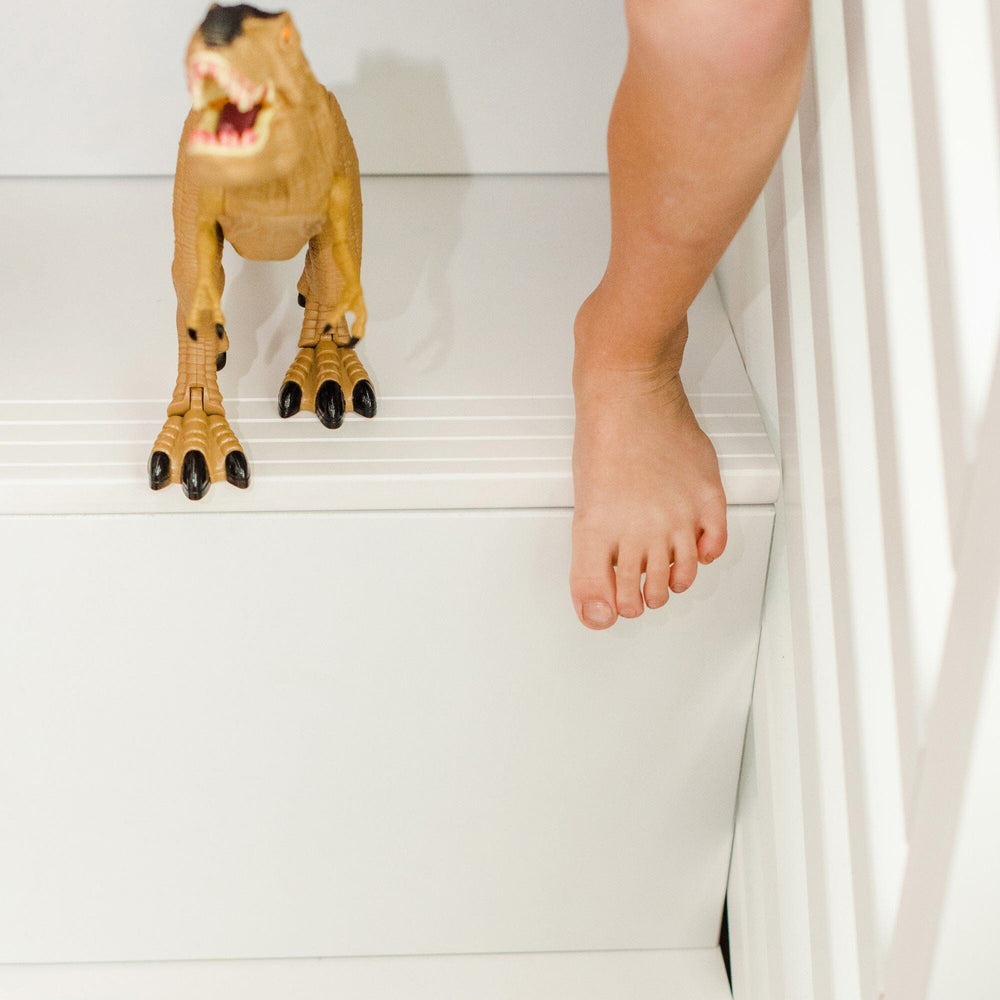 Child playing with dinosaur toy on white staircase.