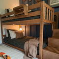 Wooden bunk bed with storage stairs and ladder, cozy dark patterned bedding, pillows and bedside lamp in a kids' bedroom with wooden toy train