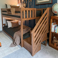 Wooden bunk bed with staircase and built-in storage in kids' bedroom with navy accent wall, cozy dark patterned bedding and globe