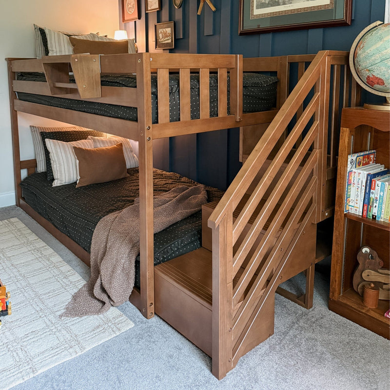 Wooden bunk bed with staircase and built-in storage in kids' bedroom with navy accent wall, cozy dark patterned bedding and globe