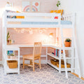 Kids loft bed with built-in L-shaped study desk and ladder in pastel pink bedroom, wooden chair, string lights, potted plants, bookshelf and woven baskets on gray geometric rug