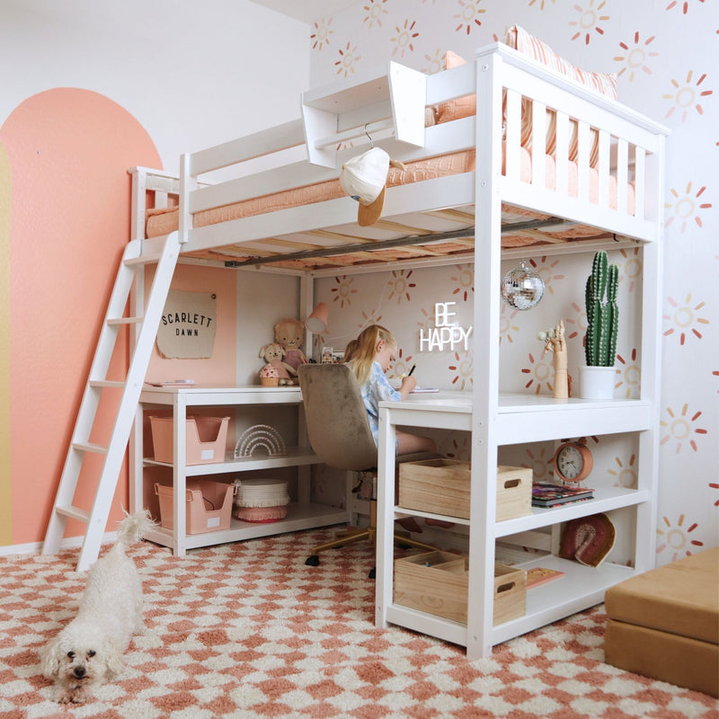 White loft bed with built-in desk and shelves in a peach-and-white girls bedroom study nook, patterned rug, cactus, toys and small white dog