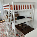 White loft bed with ladder and rust-orange velvet bedding above a built-in white desk, green velvet swivel chair, brass lamp and wicker storage baskets in a bright kids' bedroom with patterned rug