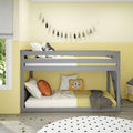 Gray bunk bed in yellow children's bedroom with tassel garland, lion throw pillow, polka-dot rug, white bedding and wood floor