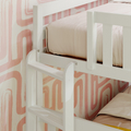 White wooden bunk bed ladder and guardrail against pink retro geometric wallpaper with soft beige bedding in a modern kids' bedroom