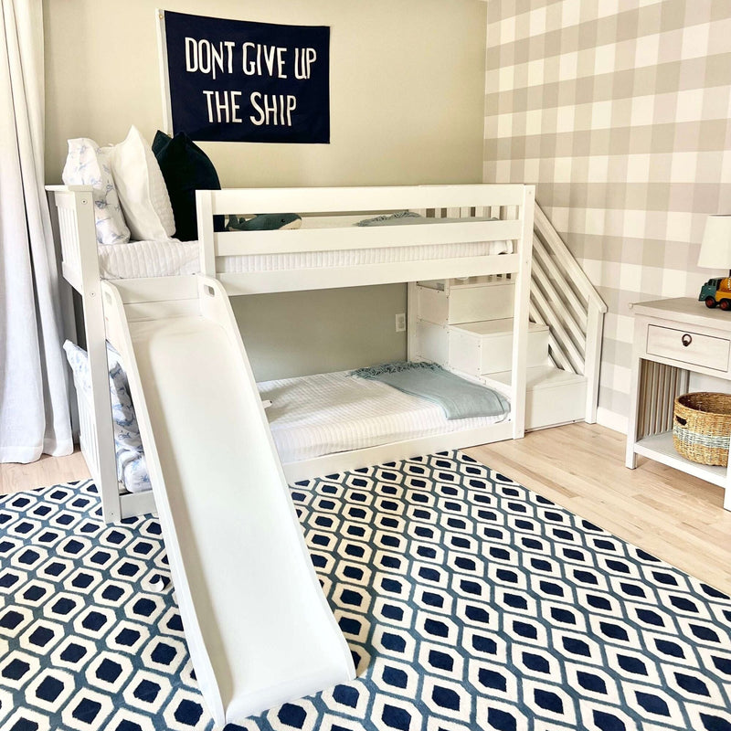 Kids bedroom with white bunk bed featuring a slide, geometric rug, and motivational "Don't Give Up the Ship" wall art.