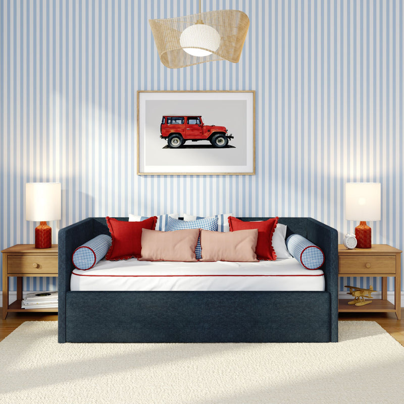 Blue striped wallpaper bedroom with navy upholstered daybed, red and blush accent pillows, framed vintage red jeep print, wooden nightstands, table lamps and woven rattan pendant light
