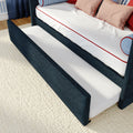 Pull-out trundle bed with navy upholstered frame, white mattress with red piping and decorative pillows on a cream textured rug
