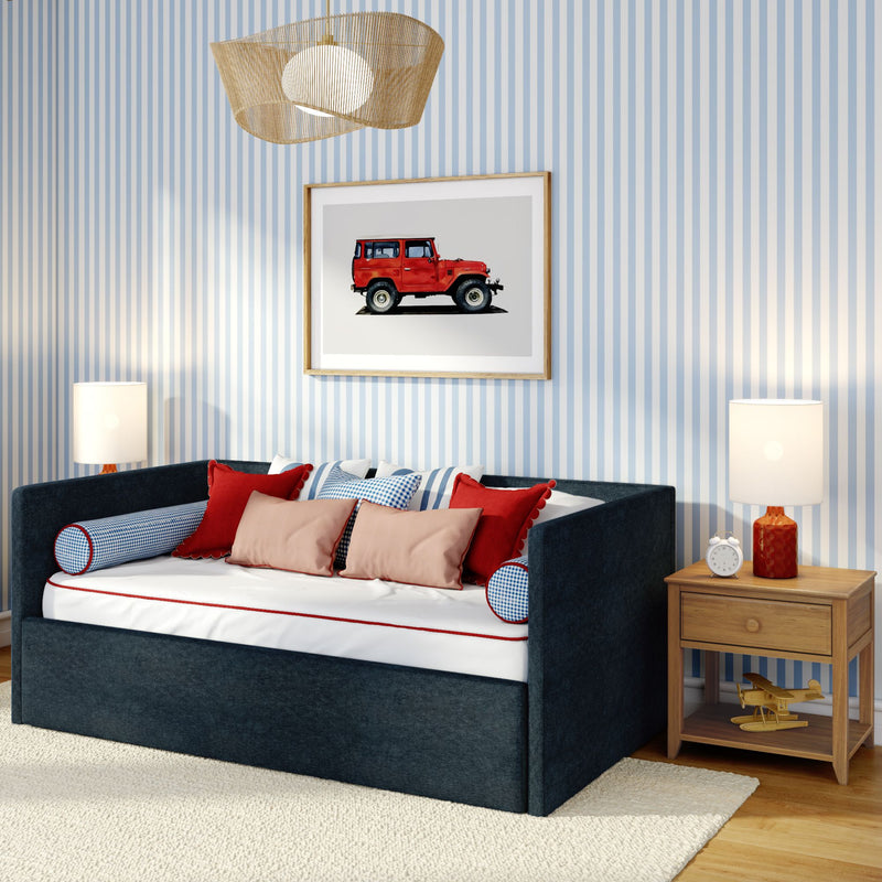 Kids bedroom with navy daybed, red and blue pillows, blue-and-white striped wallpaper, framed vintage red jeep print, wooden nightstand with alarm clock and toy airplane, rattan pendant light