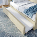 Modern upholstered bed with pull-out trundle drawer, white linens and blue throw on patterned rug — bedroom storage solution
