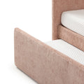 Blush pink upholstered bed frame with textured fabric and white quilted mattress corner, modern platform bed headboard and footboard detail