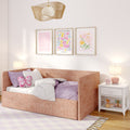 Cozy pastel pink children’s bedroom with upholstered daybed, butterfly pillow, floral wall art, woven pendant light and white nightstand with pink alarm clock