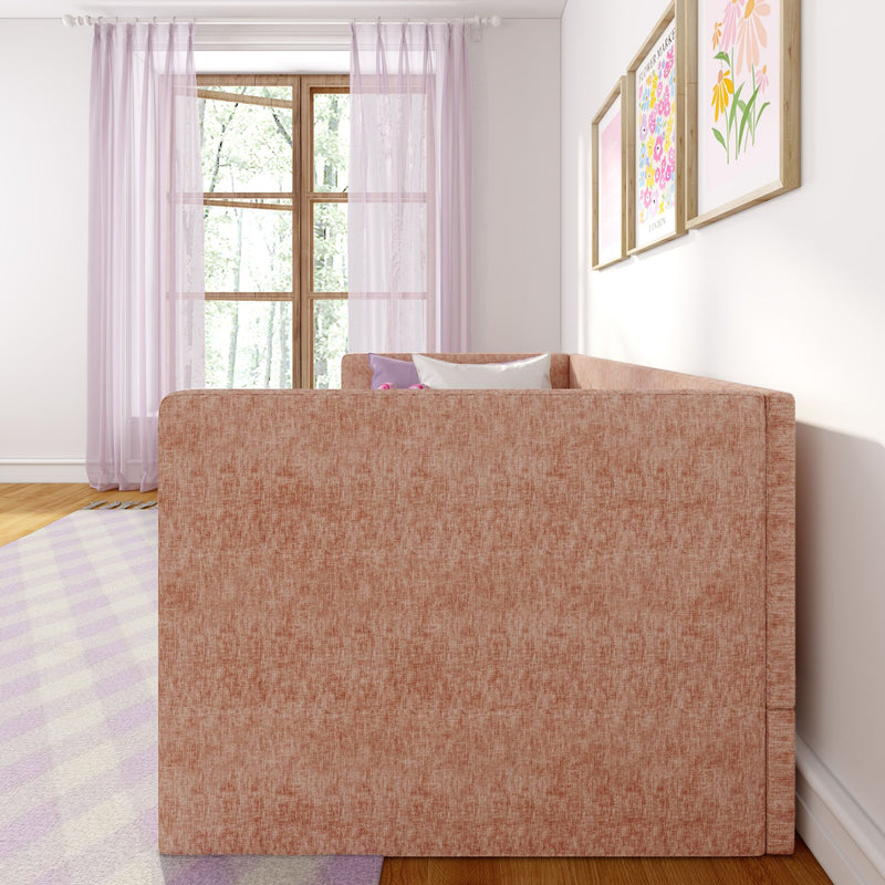 Bright pastel living room with blush pink upholstered sofa, sheer lavender curtains over wooden window, floral framed prints, decorative pillows and pastel area rug