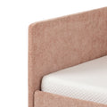 Close-up of blush pink upholstered fabric bed frame headboard and footboard with white quilted mattress