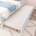 White trundle bed with pull-out mattress under a white twin bed in a pastel kids’ bedroom with blue throw blanket and pink patterned wallpaper