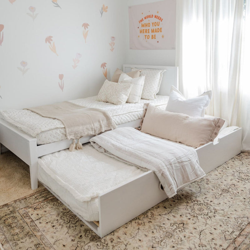 Cozy children's bedroom with a pull-out trundle bed, white bedding, and floral wall design.