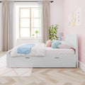 Pastel pink kids' bedroom with white twin storage bed, blue and pink pillows, light wood chevron floor, large window and potted plant