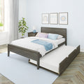 Grey wood platform bed with pull-out trundle, white quilt and pastel pillows, bedside table with lamp, potted plant and framed nursery art on a light blue patterned wall in a bright modern kids' bedroom