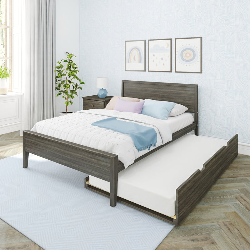 Grey wood platform bed with pull-out trundle, white quilt and pastel pillows, bedside table with lamp, potted plant and framed nursery art on a light blue patterned wall in a bright modern kids' bedroom