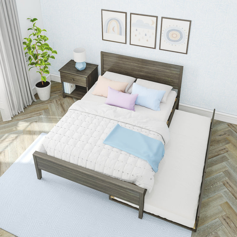 Modern bedroom with dark wooden bed frame and pull-out trundle, white quilted bedding and pastel pillows, wooden nightstand with blue lamp, potted plant, framed wall art and herringbone hardwood floor