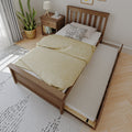 Wooden trundle bed with yellow duvet and pull-out mattress in bright modern bedroom with wooden nightstand and potted plant